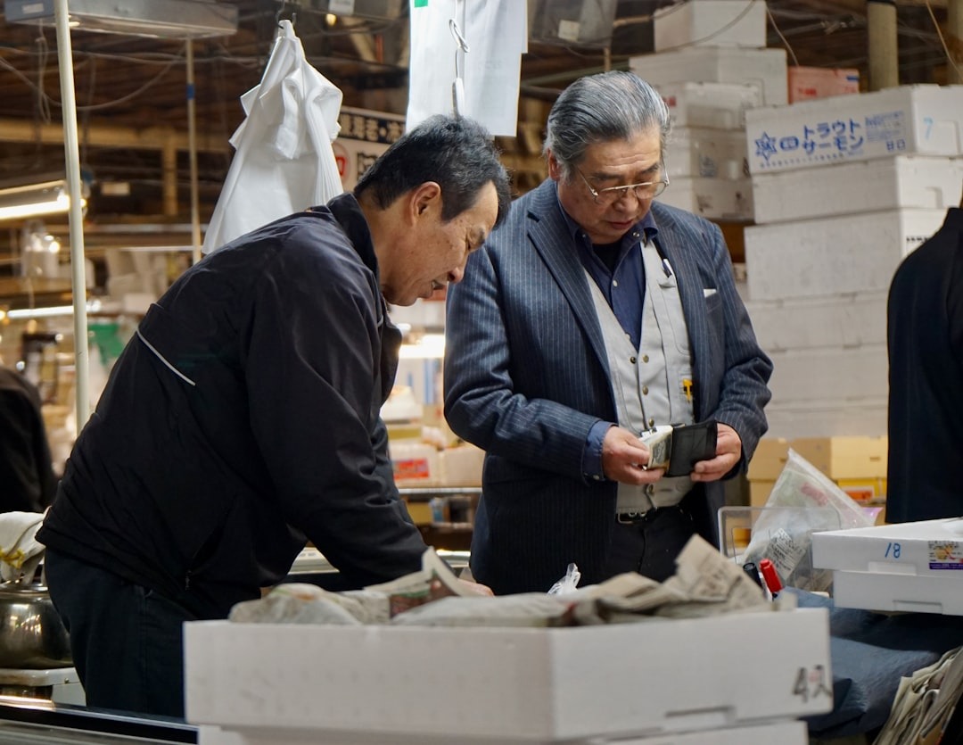 Men exchange money in a busy market with Japanese boxes.